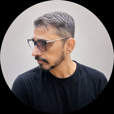 Man with gray hair and beard wearing black t-shirt and sunglasses against white circular background