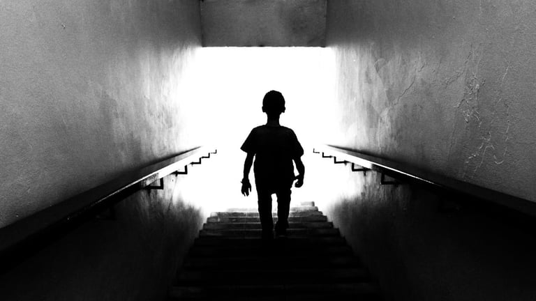 Silhouette of a person climbing stairs toward bright light in a dark concrete tunnel