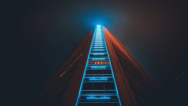 Tall modern building photographed from below at night with blue neon lighting on the facade, creating a dramatic upward perspective against a dark sky.