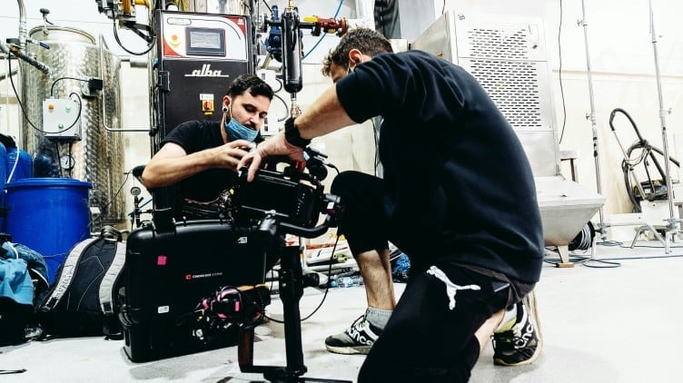 Two technicians adjusting a professional cinema camera in a studio workshop setting with equipment visible in the background