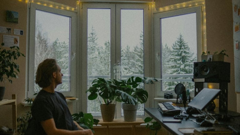 Person sitting at desk with computer, large windows showing snowy forest and evergreen trees in background